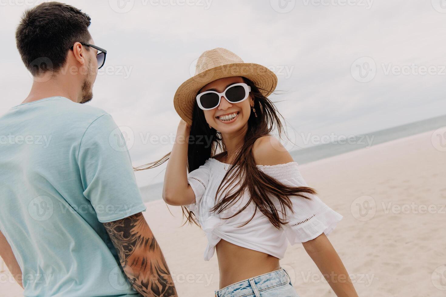 Happy young woman looking at camera while spending time on the beach with her boyfriend photo