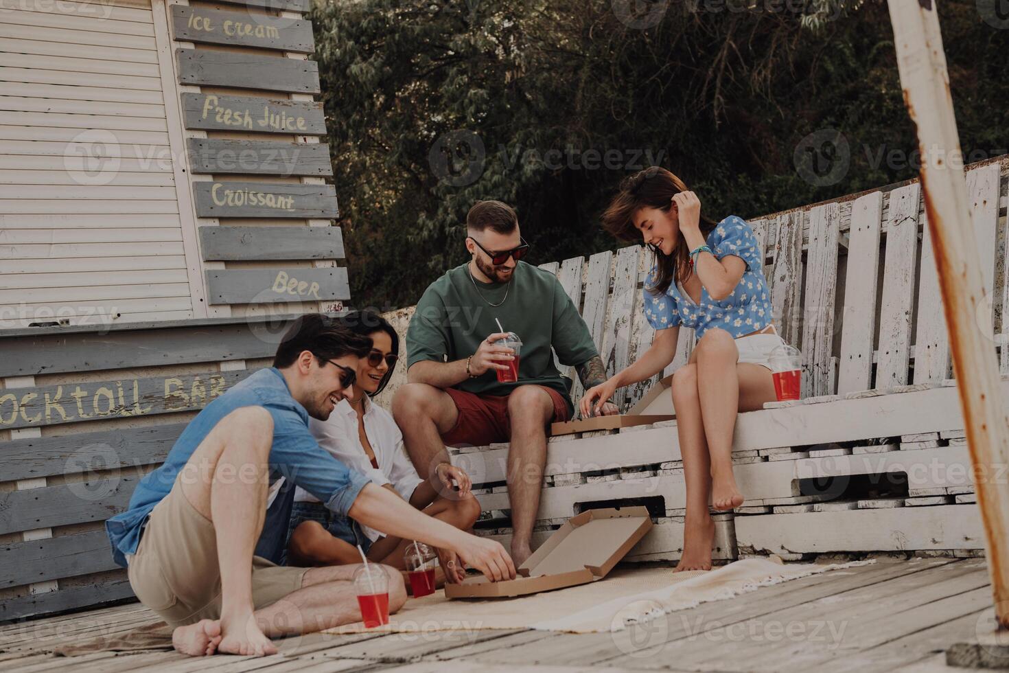 Group of happy friends enjoying food and drinks while relaxing near the beach cafe together photo
