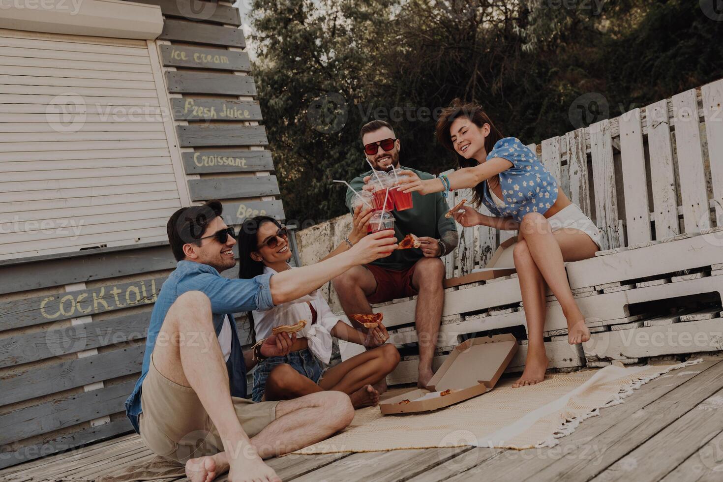Group of friends toasting with cocktails while enjoying food and drinks outdoors together photo