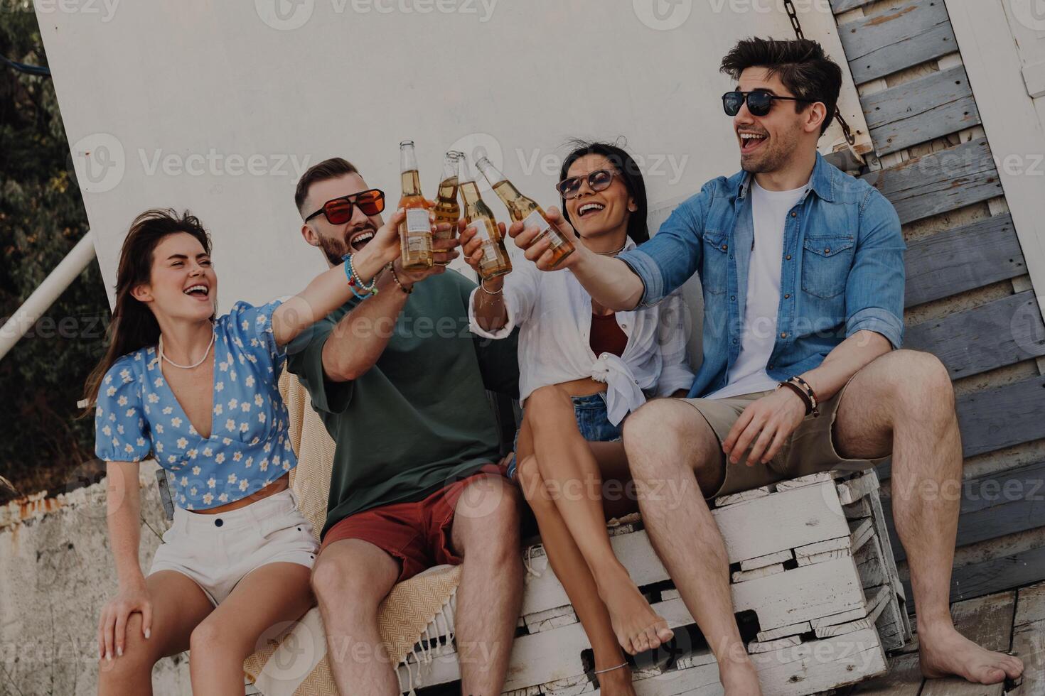 Group of joyful young friends toasting with beer while spending carefree time outdoors together photo