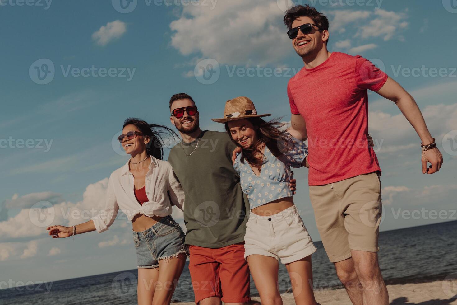 Group of happy young friends bonding and smiling while spending time on the beach together photo