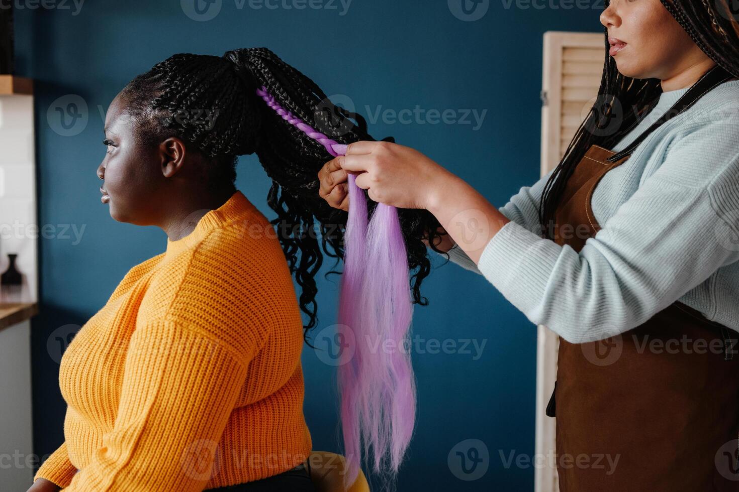 Close-up of confident hairdresser braiding hair to a young African woman in salon photo