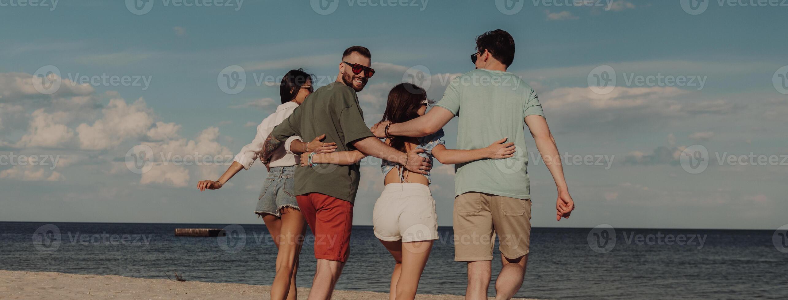 Rear view of joyful young people walking to the sea by the beach photo