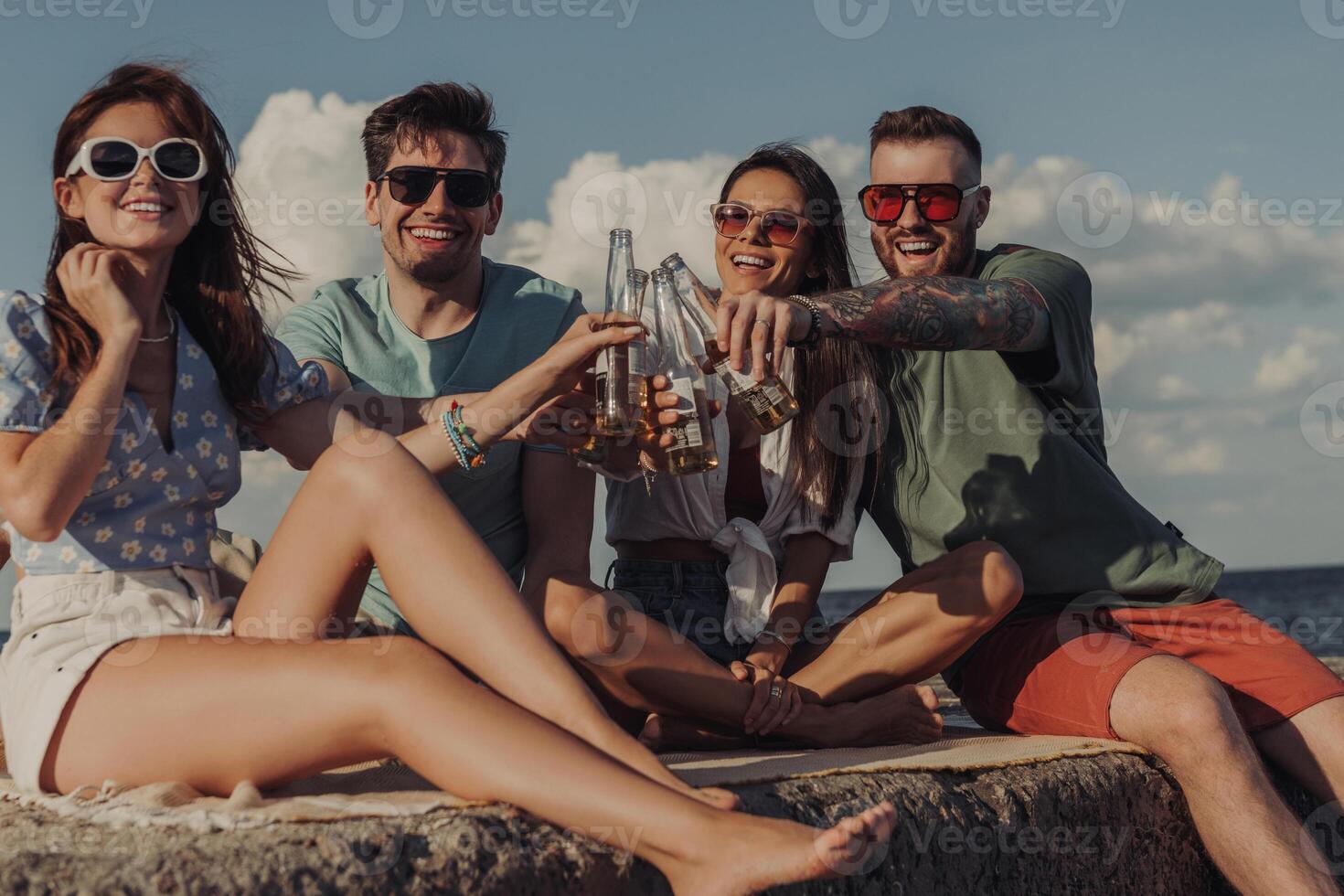 Group of happy young friends toasting with beer while spending carefree time seaside together photo