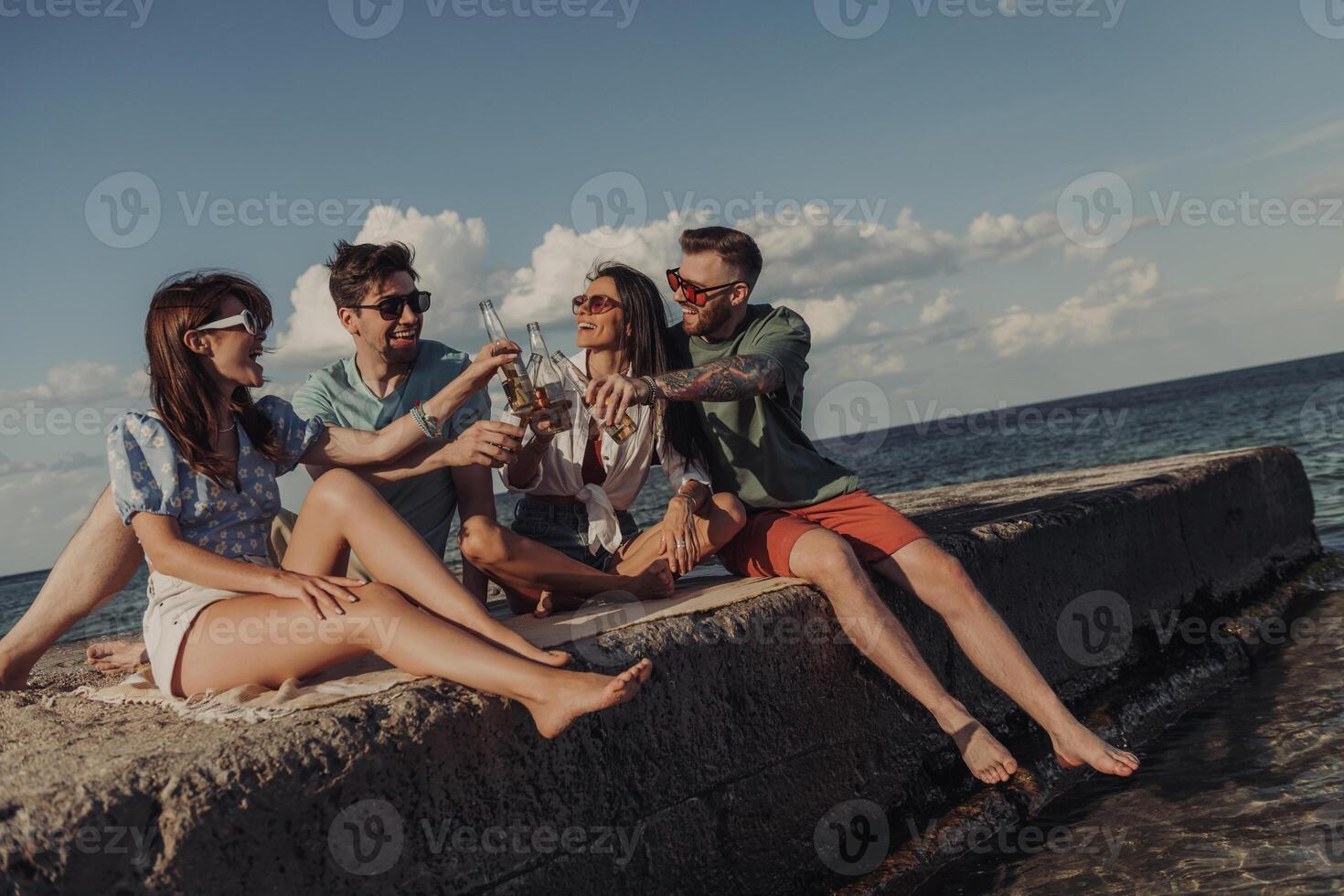 Group of young friends toasting with beer and smiling while spending time seaside together photo