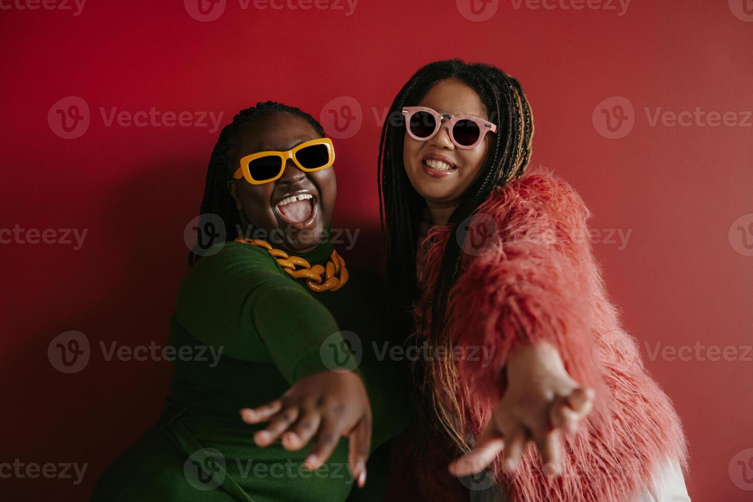 Two joyful plus size African woman with braided hair stretching out hands on red background together photo