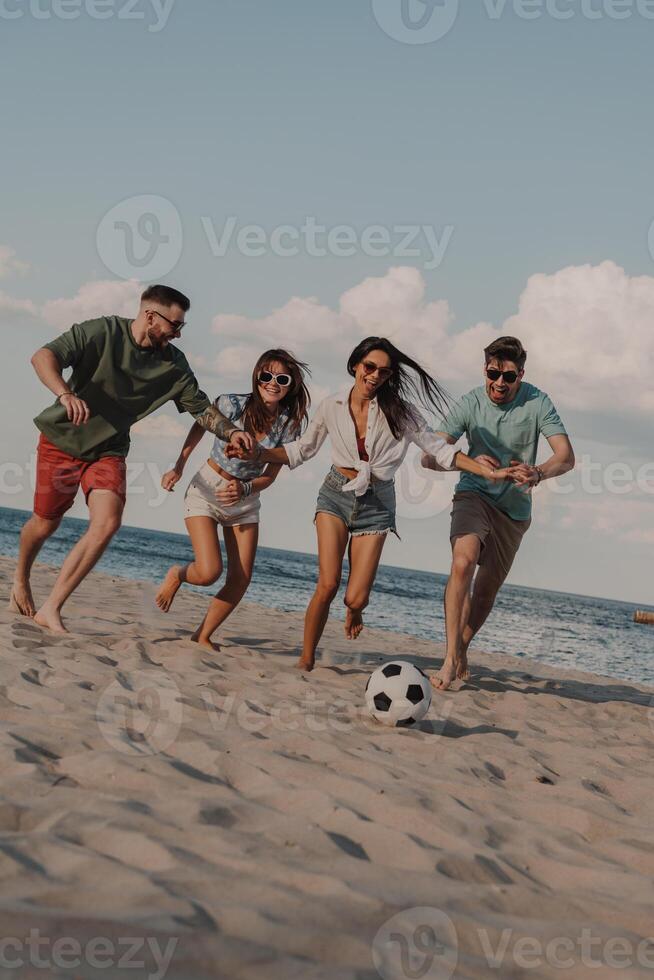 Group of happy young people spending carefree time together while playing beach soccer photo