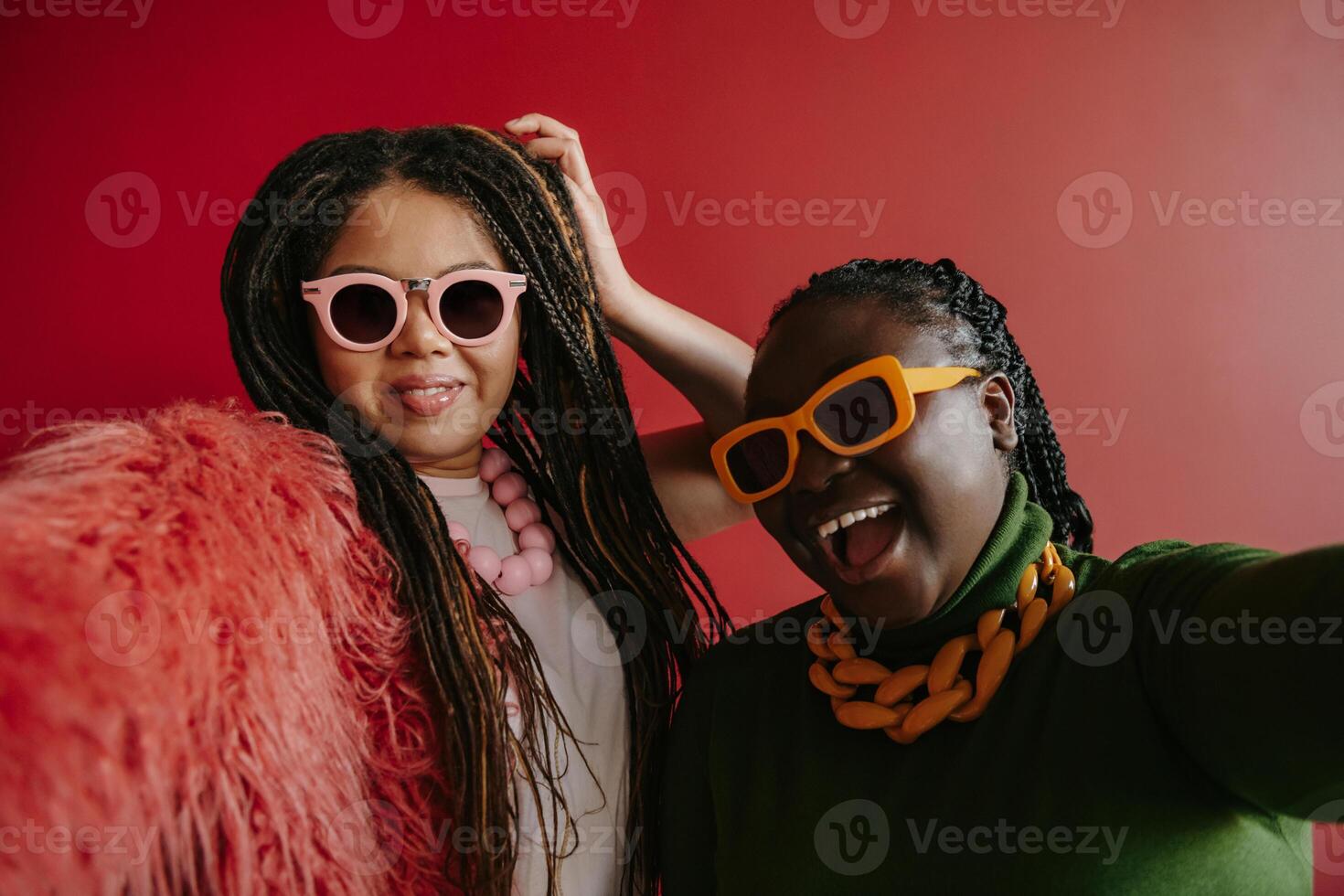 Two joyful plus size African woman with braided hair making selfie on red background together photo