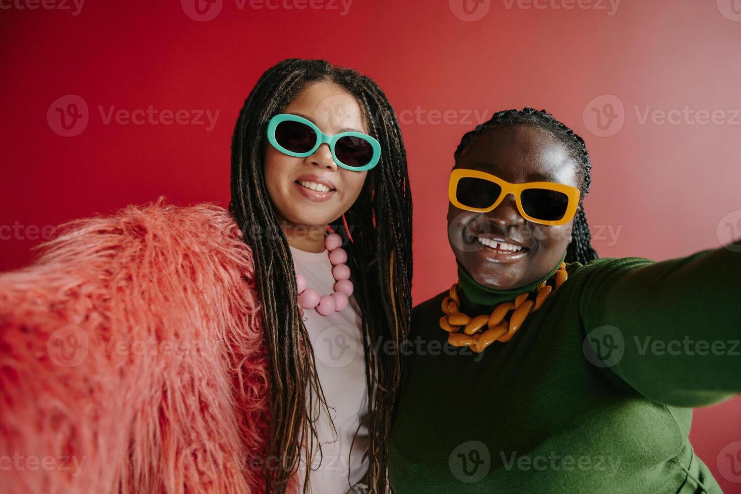 Two happy plus size African woman with braided hair making selfie on red background together photo