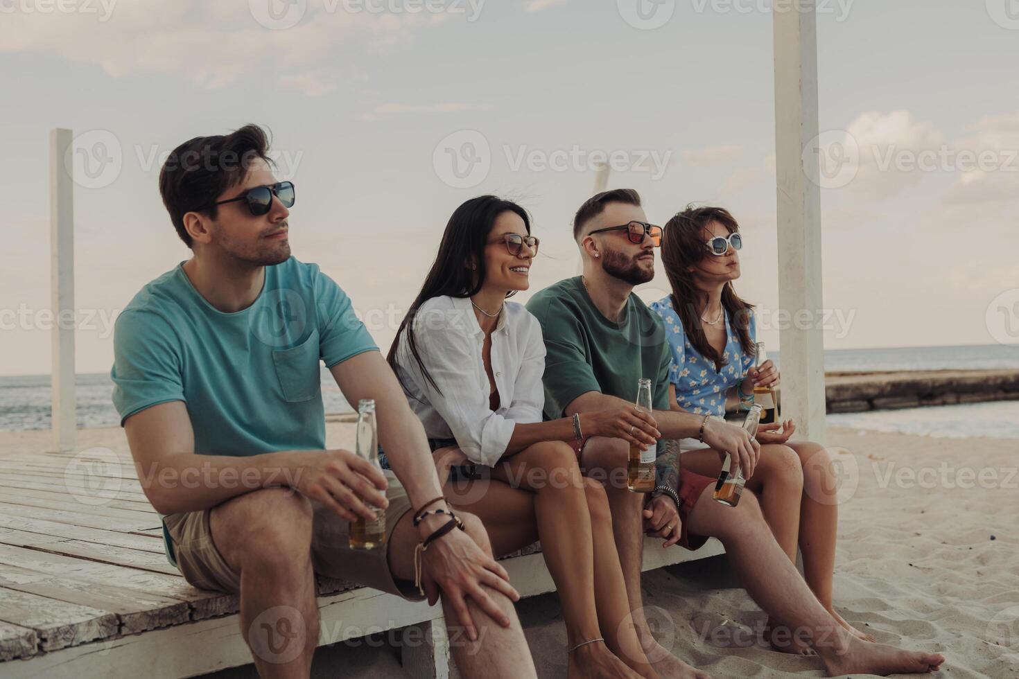 Four beautiful young people enjoying cold beer while spending carefree time on the beach together photo