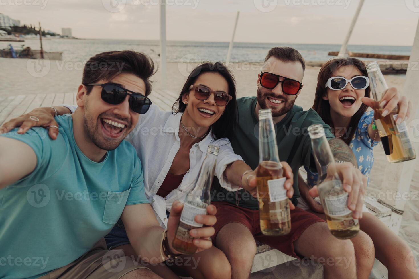 Group of cheerful young people making selfie while enjoying beer on the beach together photo