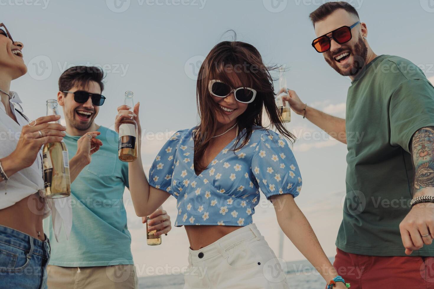 Group of beautiful young people enjoying beer and smiling while dancing on the beach together photo