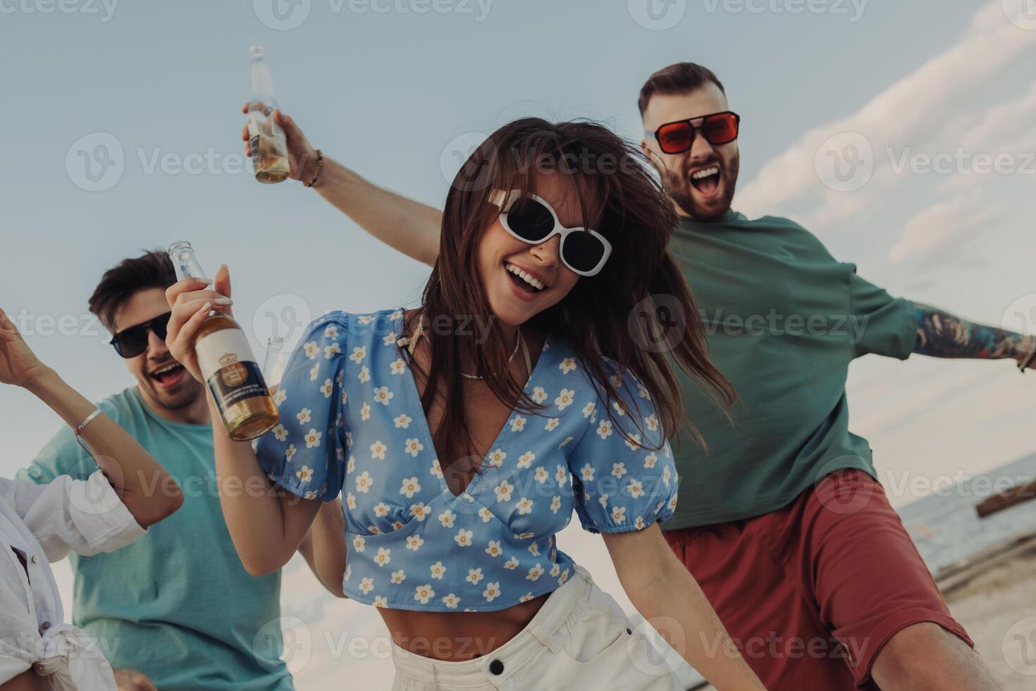 Group of happy young people enjoying beer and having fun while dancing on the beach together photo