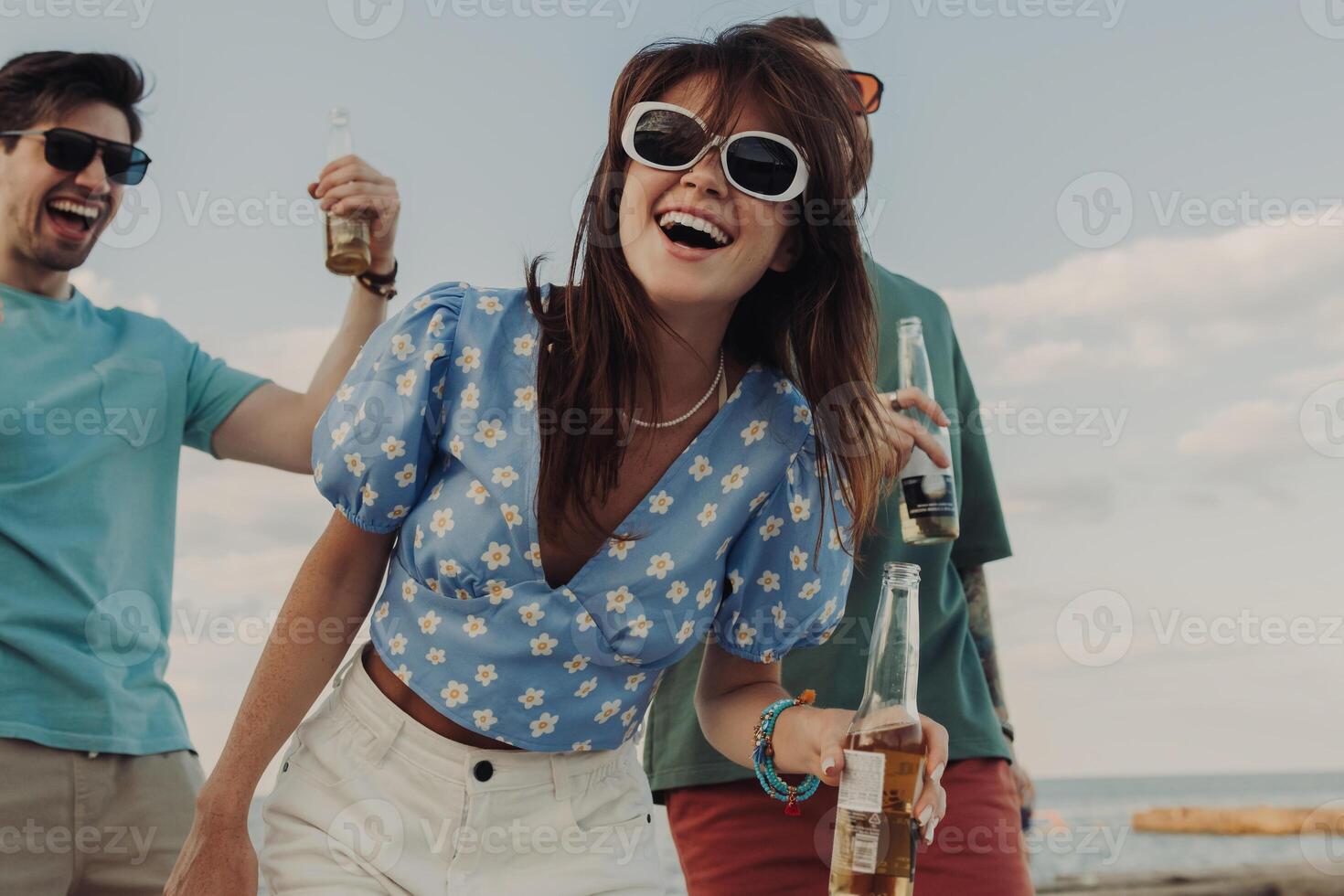 Group of happy friends enjoying beer and dancing while having fun on the beach together photo