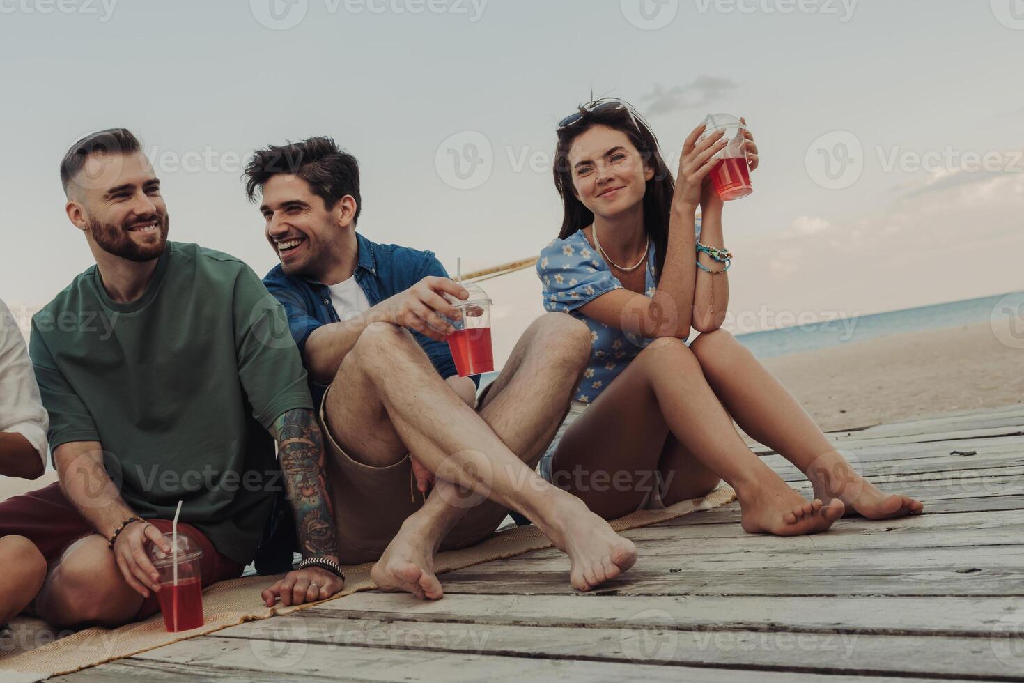 Beautiful young people enjoying summer cocktails while spending time on the beach together photo