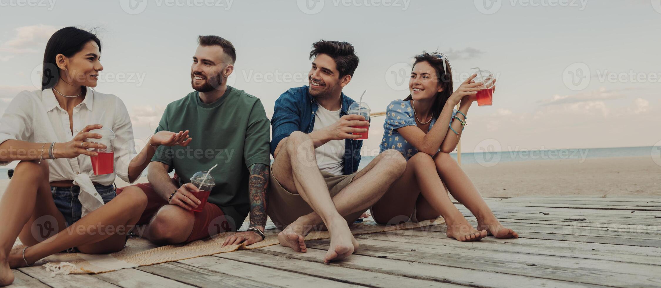 Four young friends enjoying summer cocktails while spending time on the beach together photo