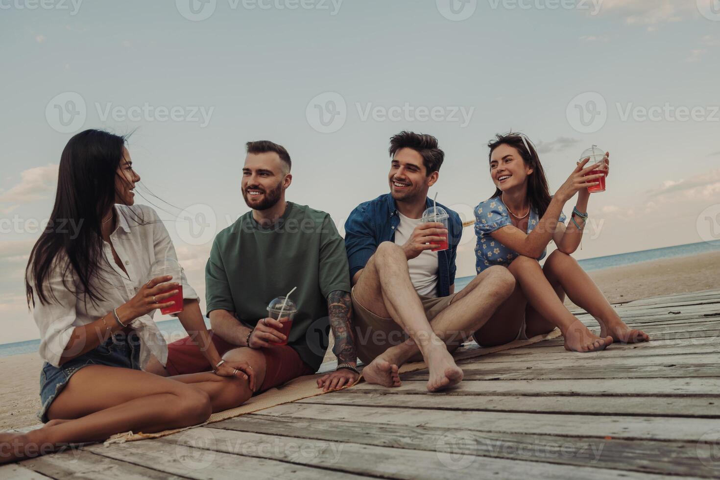 Group of young people talking and smiling while enjoying refreshing cocktails on the beach together photo