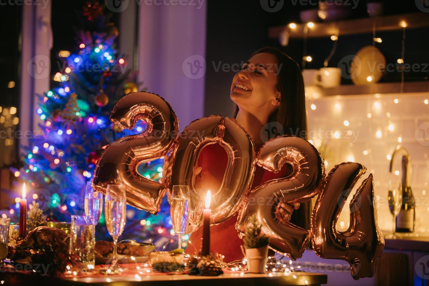 Smiling young woman holding 2024 numbers while enjoying New Year Eve at decorated home photo