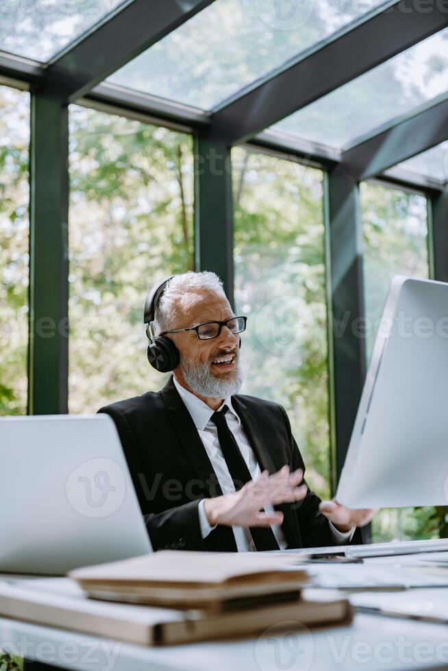 Confident mature businessman in headphones using computer while having web conference from office photo