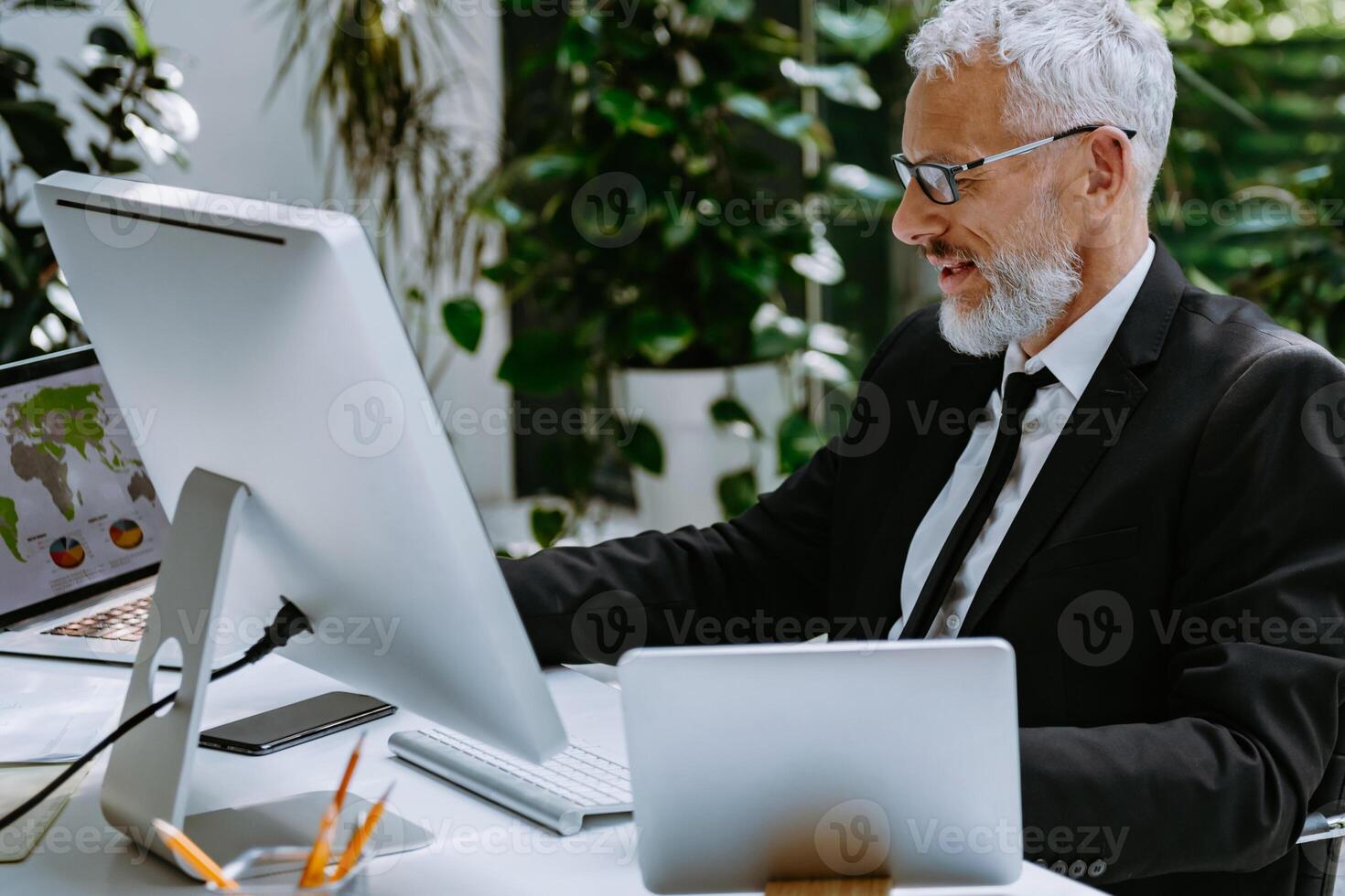 Confident mature man in formalwear using technologies while working in the modern office photo
