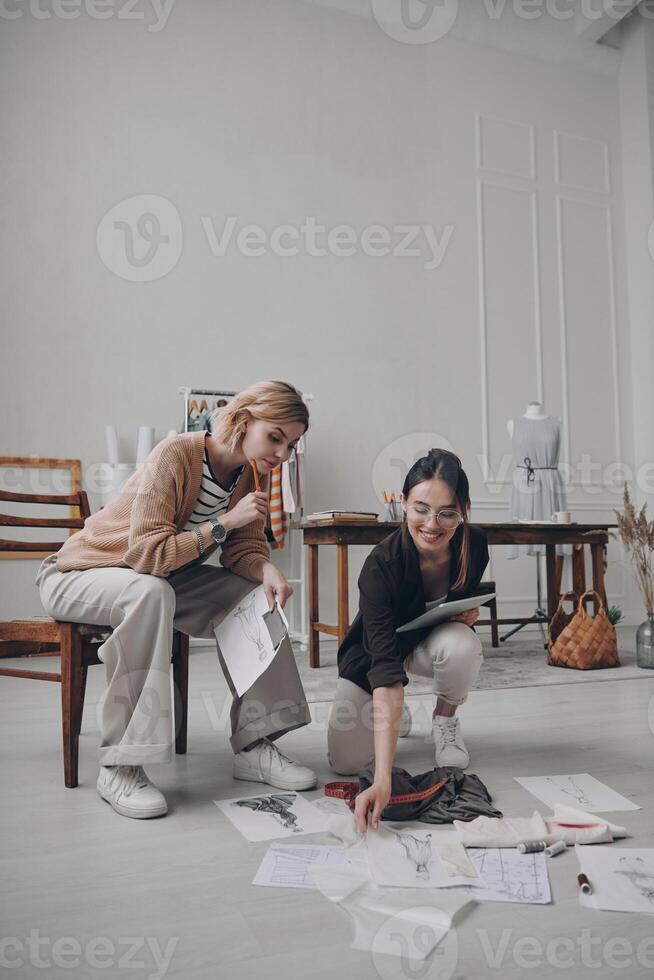 Two confident female fashion designers examining sketches while working in workshop photo