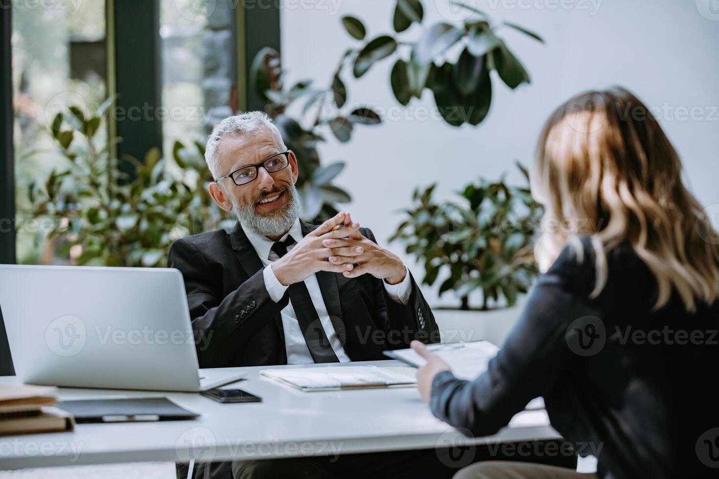Happy mature man in formalwear interviewing job candidate while sitting at the desk in office photo