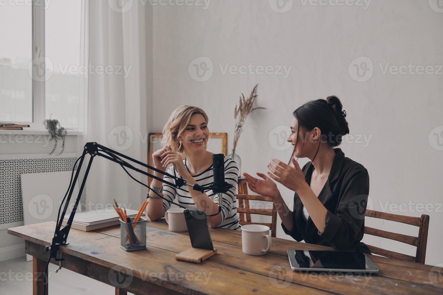 Two beautiful young women talking and smiling while co-hosting a live broadcast in studio photo