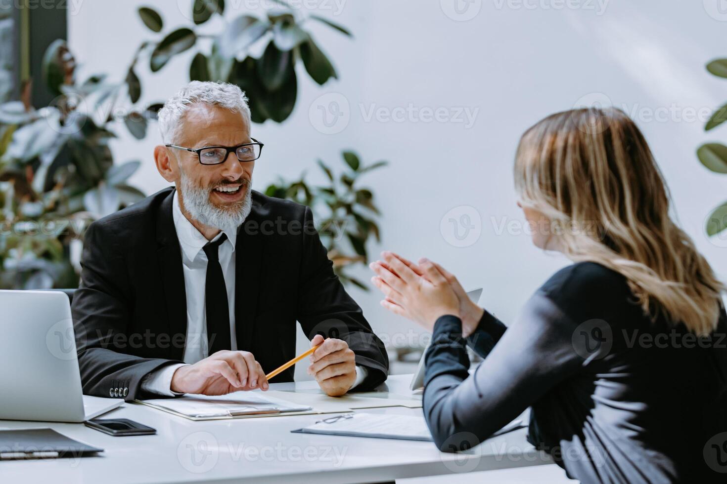 Happy mature man in formalwear interviewing job candidate while sitting at the office desk together photo