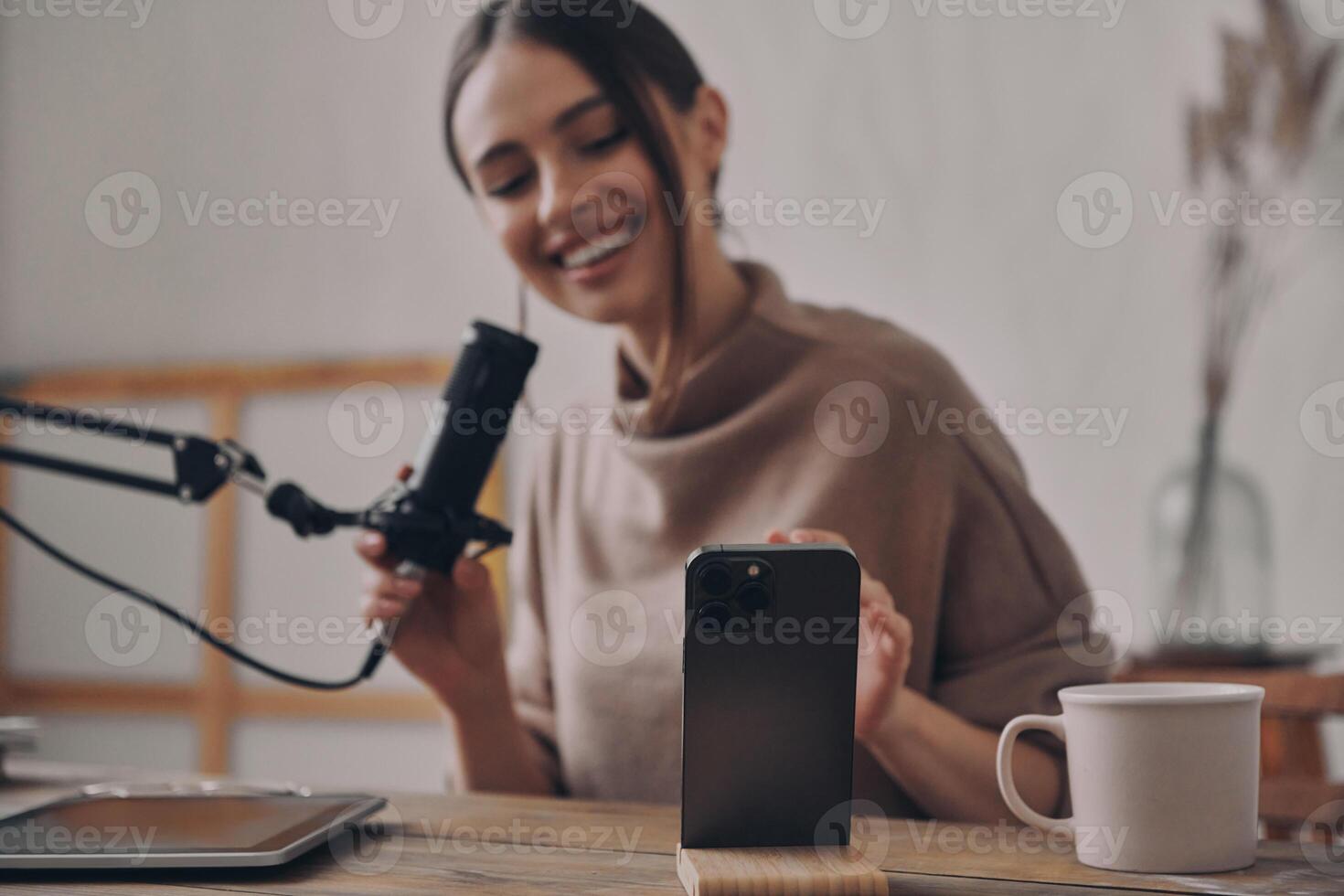 Happy young woman recording podcast while sitting at her workplace in studio photo
