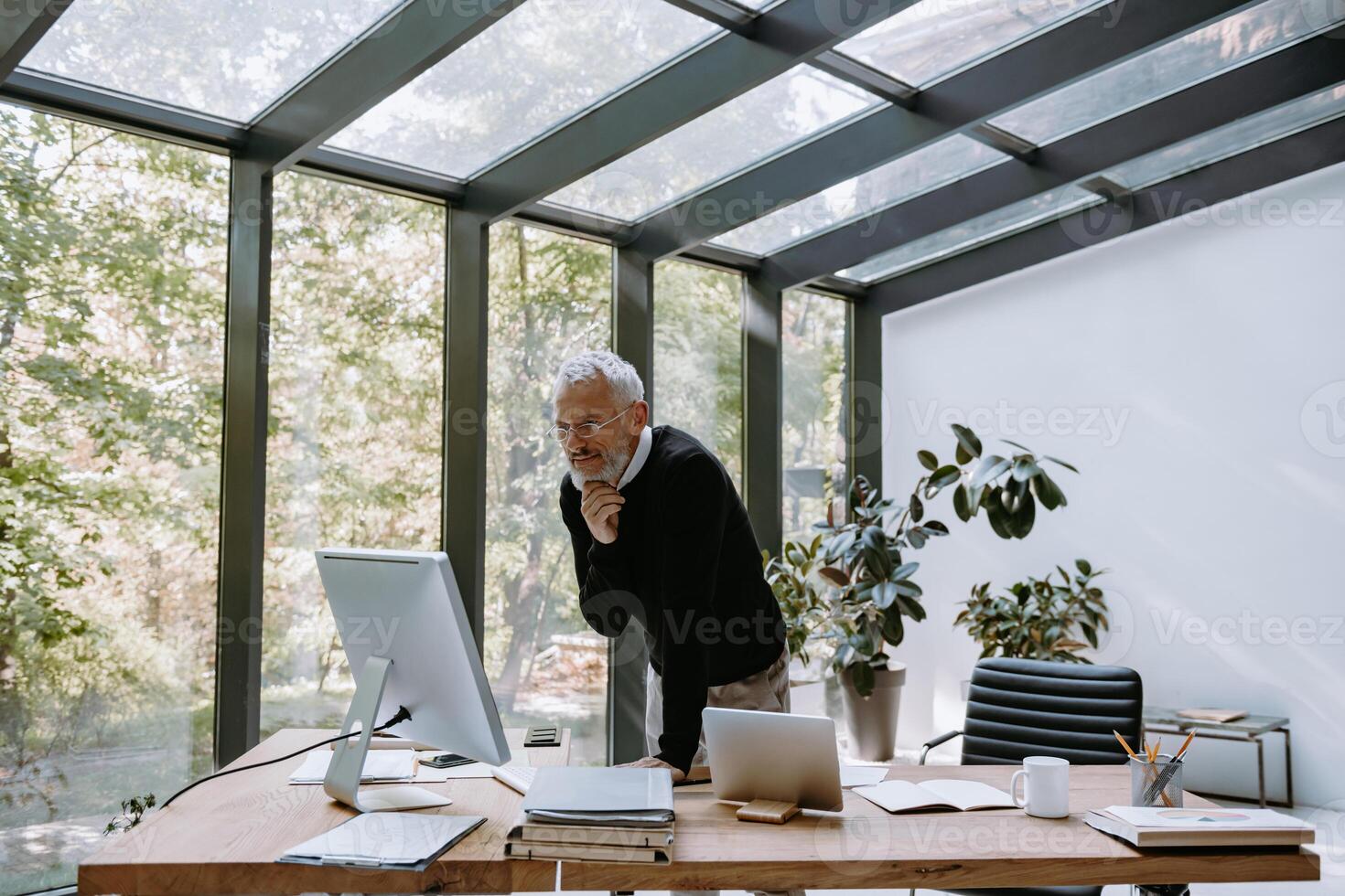 Thoughtful mature man looking at computer monitor while working in the modern office photo