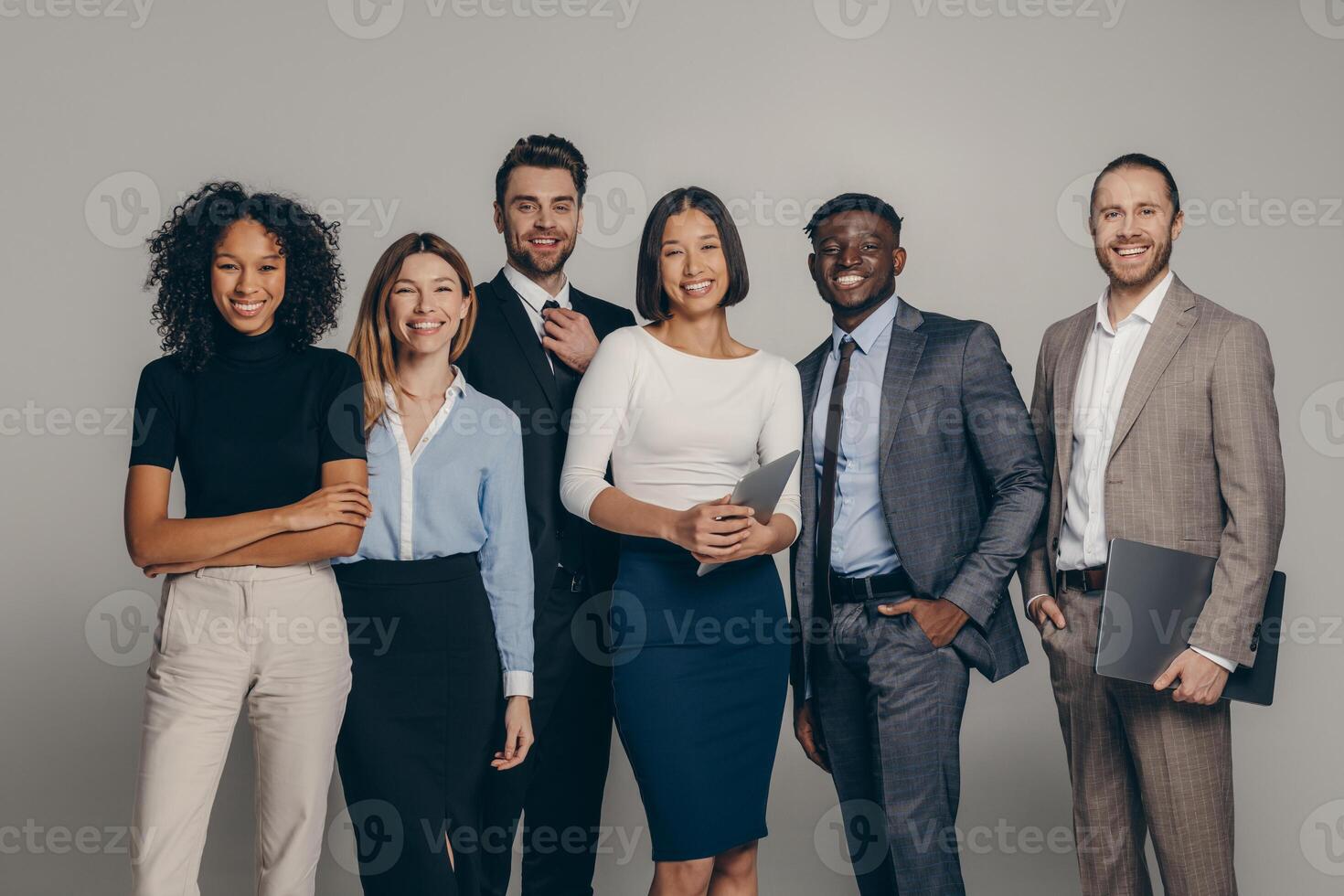 Happy young business team in formalwear looking at camera while standing on beige background photo