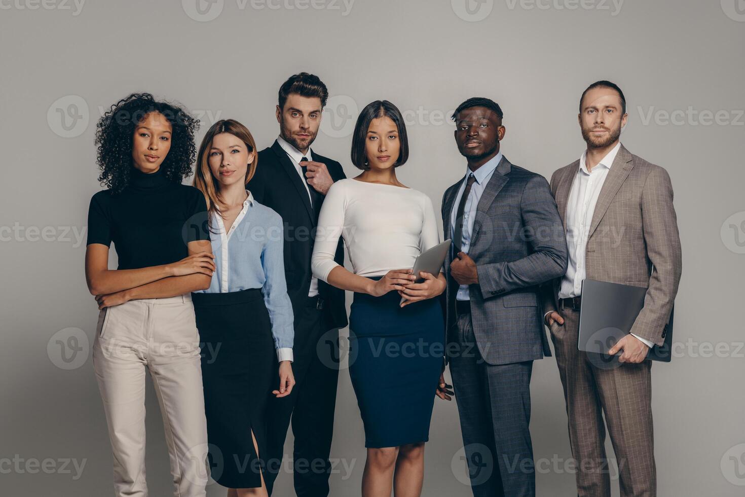 Confident young business people looking at camera while standing on beige background together photo