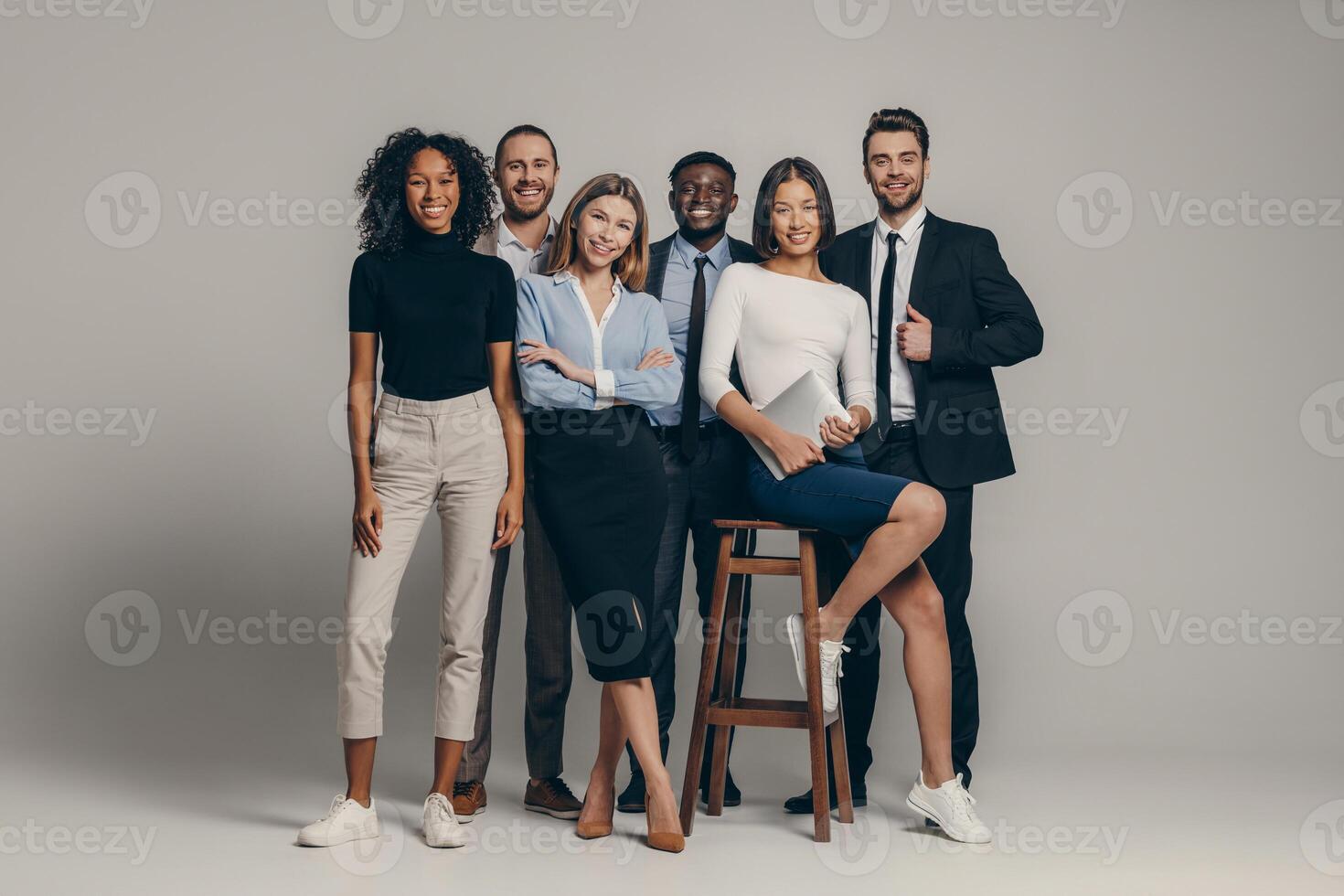 Happy young business team in formalwear looking at camera while standing on beige background photo