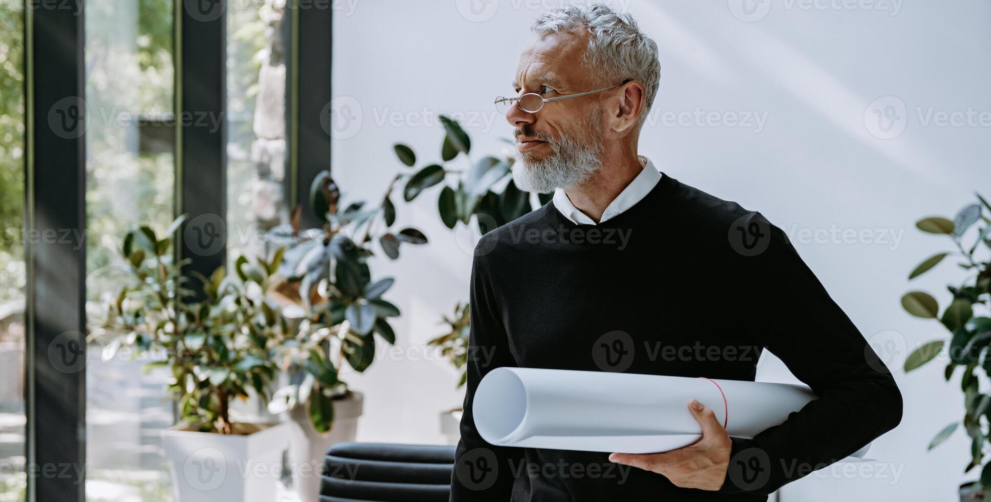 Confident mature architect carrying blueprint while standing in the creative office photo
