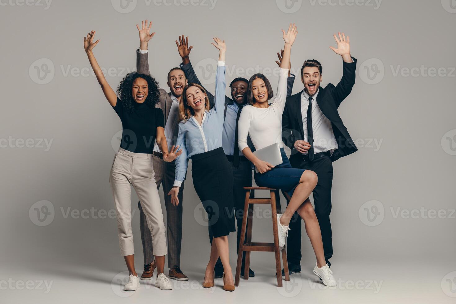 Joyful young business team in formalwear gesturing while standing on beige background photo