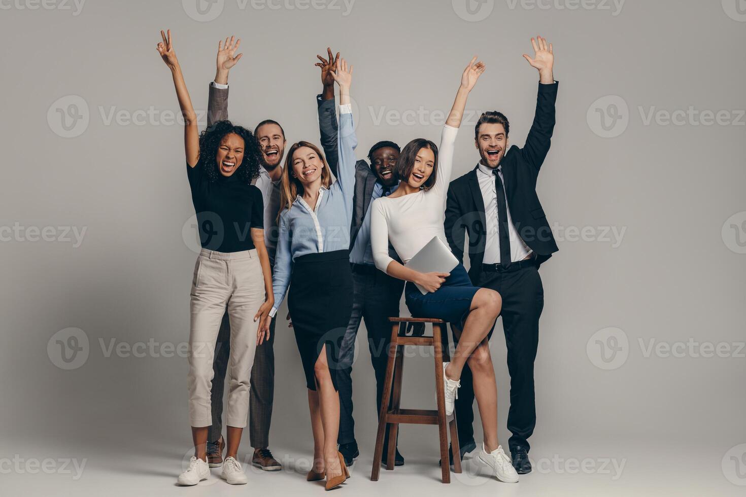 Happy young business team in formalwear gesturing while standing on beige background photo
