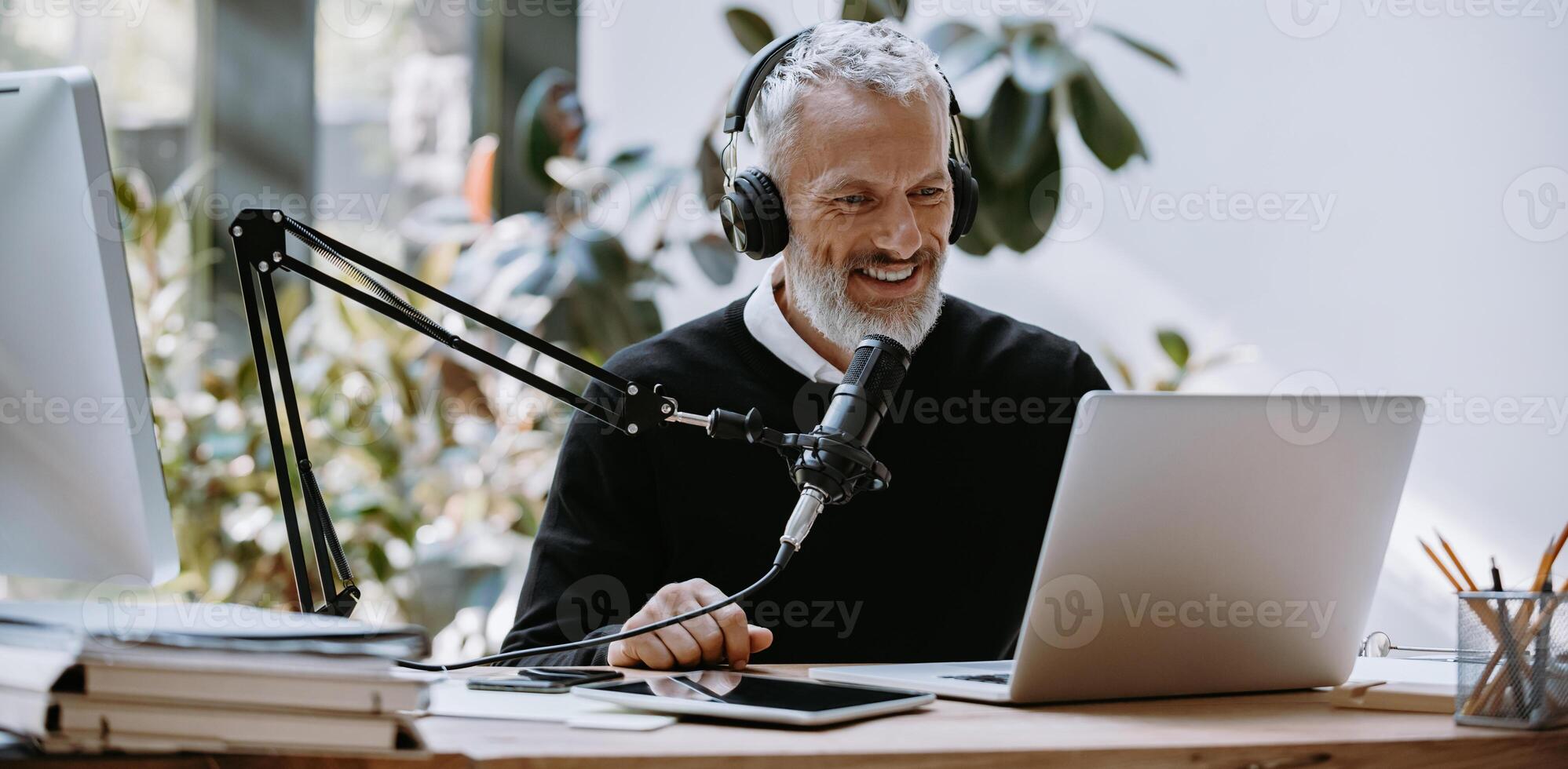 Cheerful mature podcaster in headphones using microphone while broadcasting from studio photo