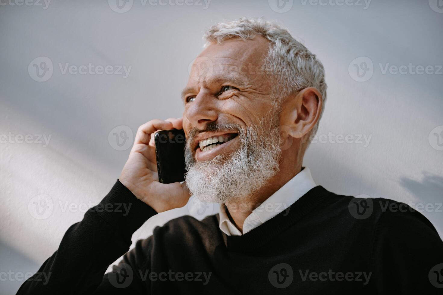 Portrait of happy senior man talking on mobile phone and smiling while standing against the wall photo
