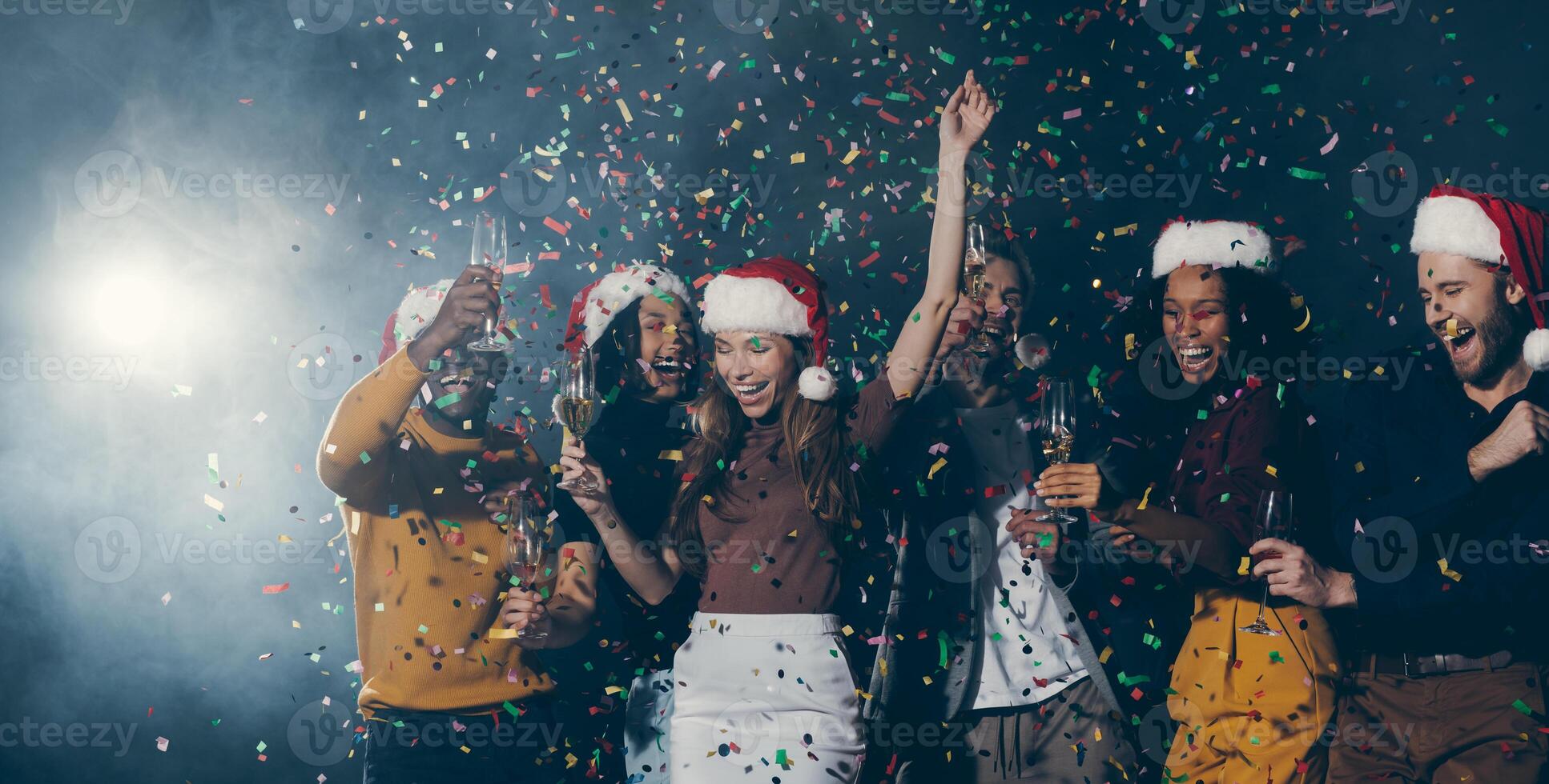 Group of young joyful people dancing and throwing confetti while enjoying New Year party in night club photo