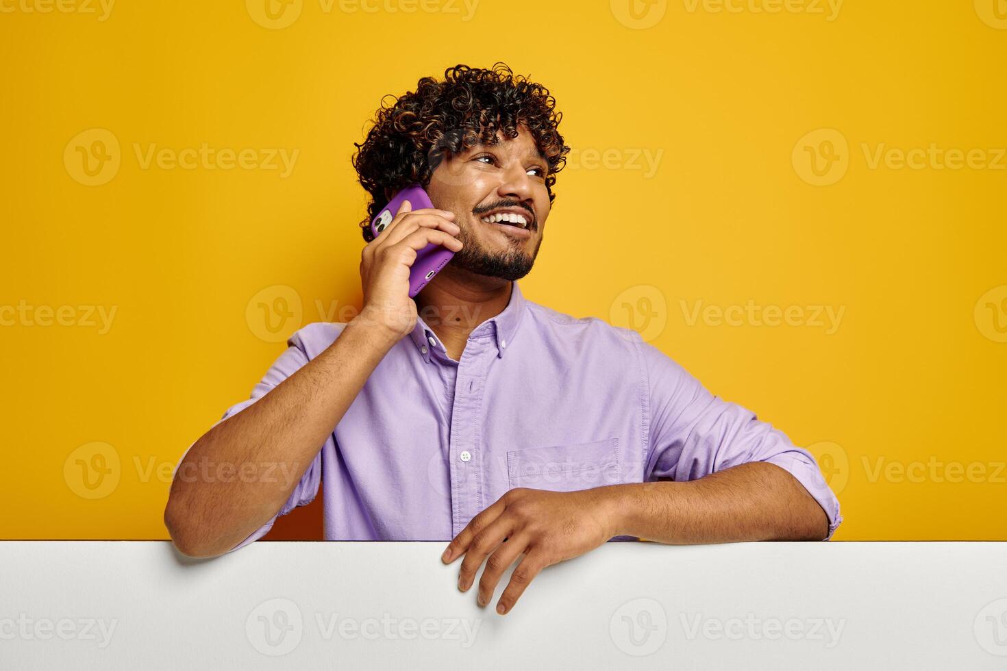 Happy Indian man leaning on the copy space and talking on phone against yellow background photo