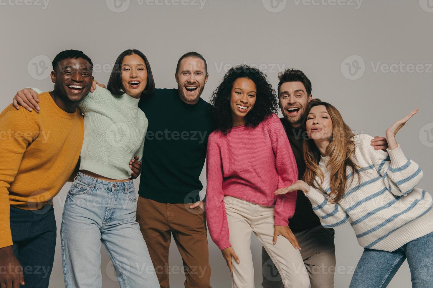 Happy young friends embracing and smiling while standing on beige background together photo