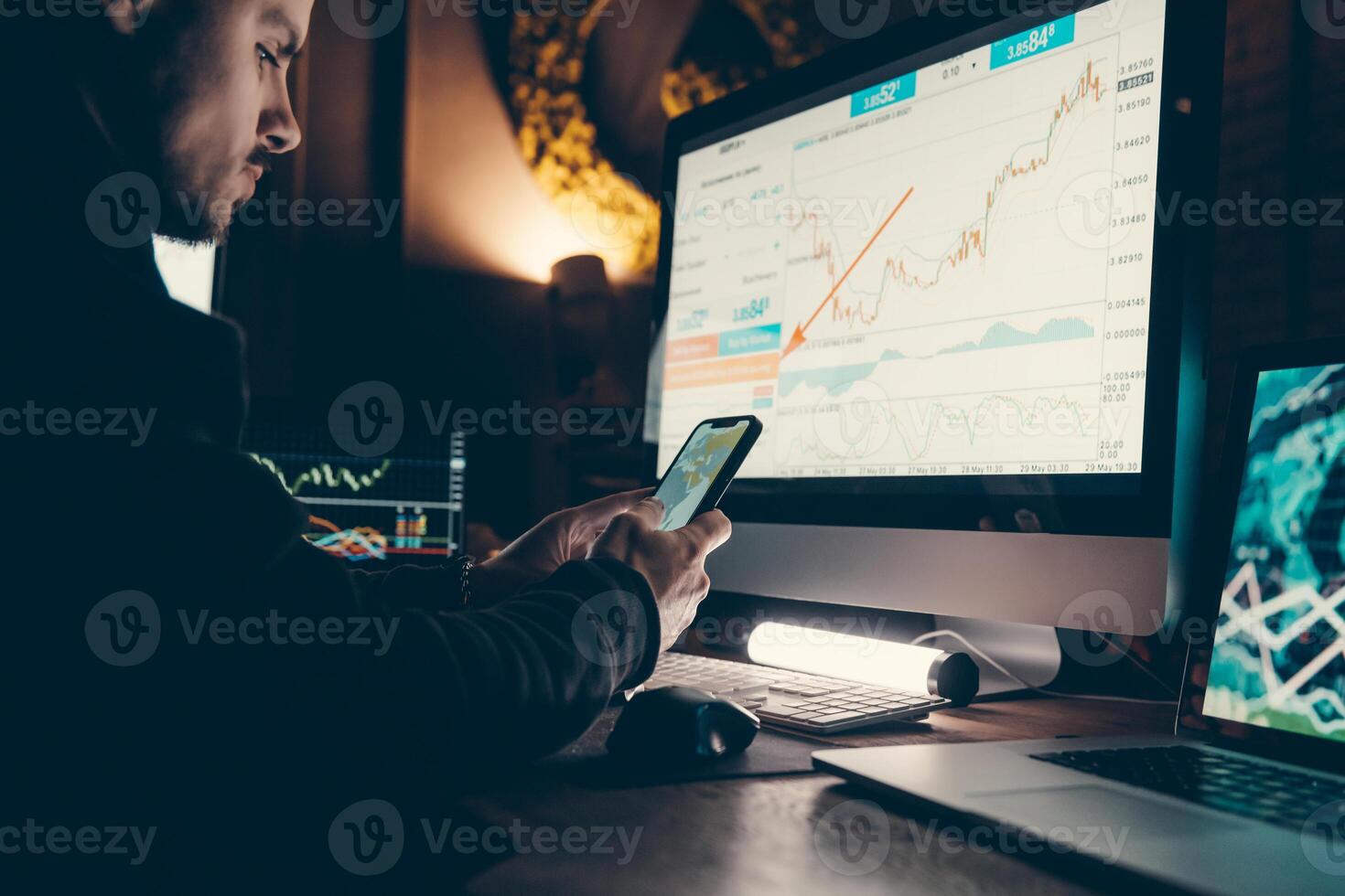 Close-up of confident young male stock trader using smart phone and computers while working late in office photo