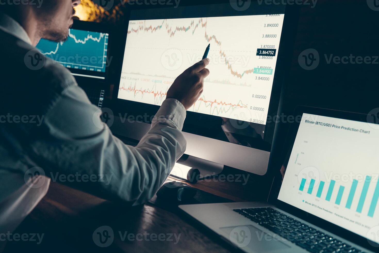 Close-up of male financial broker pointing computer monitor while analyzing stock market graph in night office photo