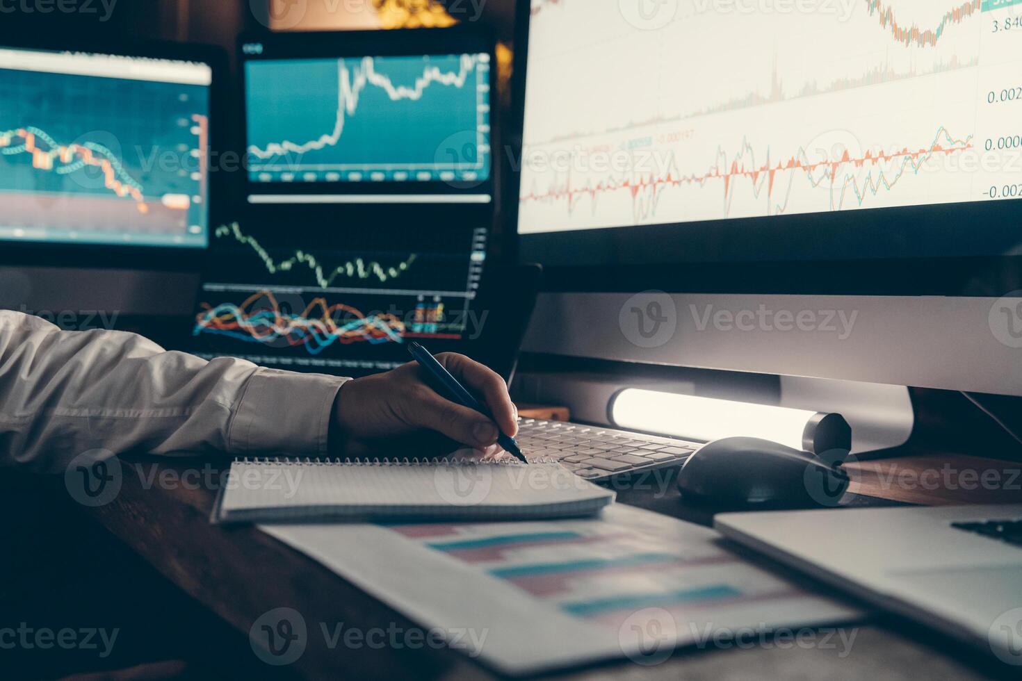 Close-up of male trader making notes and using computers while analyzing stock market data in night office photo