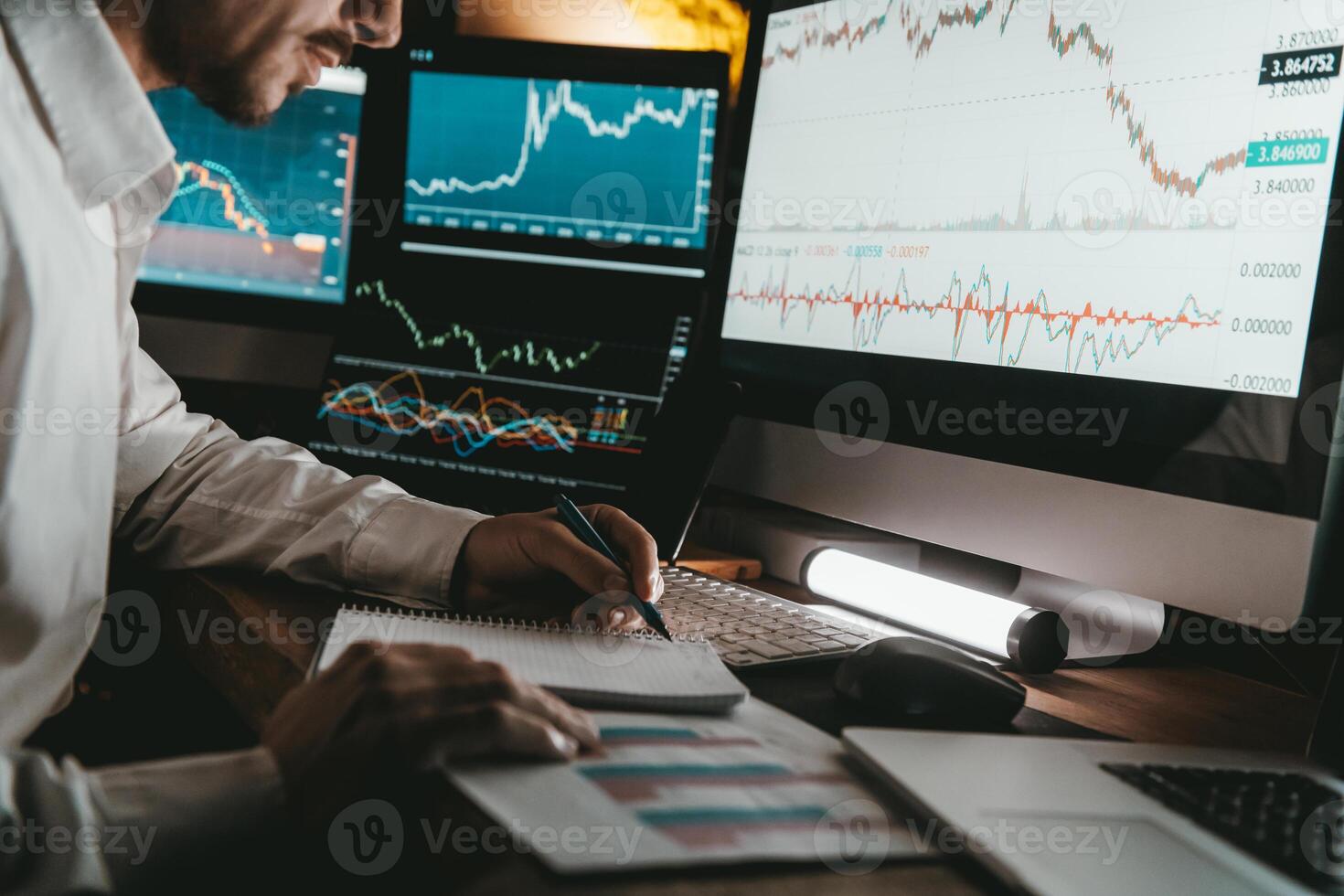 Close-up of male trader making notes and using computers while analyzing stock market data in night office photo