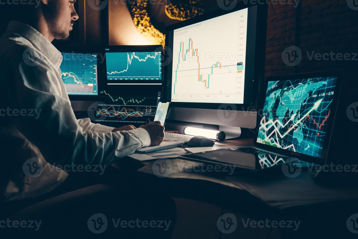 Male trader analyzing stock market data while sitting at the office workstation with multiple computers photo