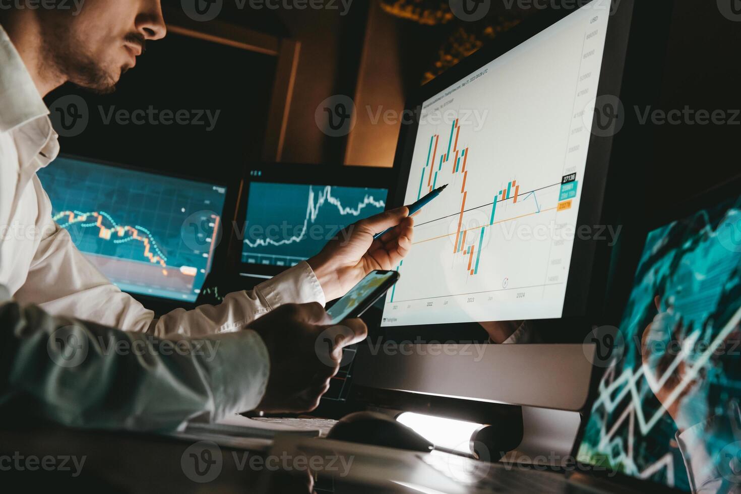 Close-up of male financial broker pointing computer monitor while analyzing stock market graph in night office photo