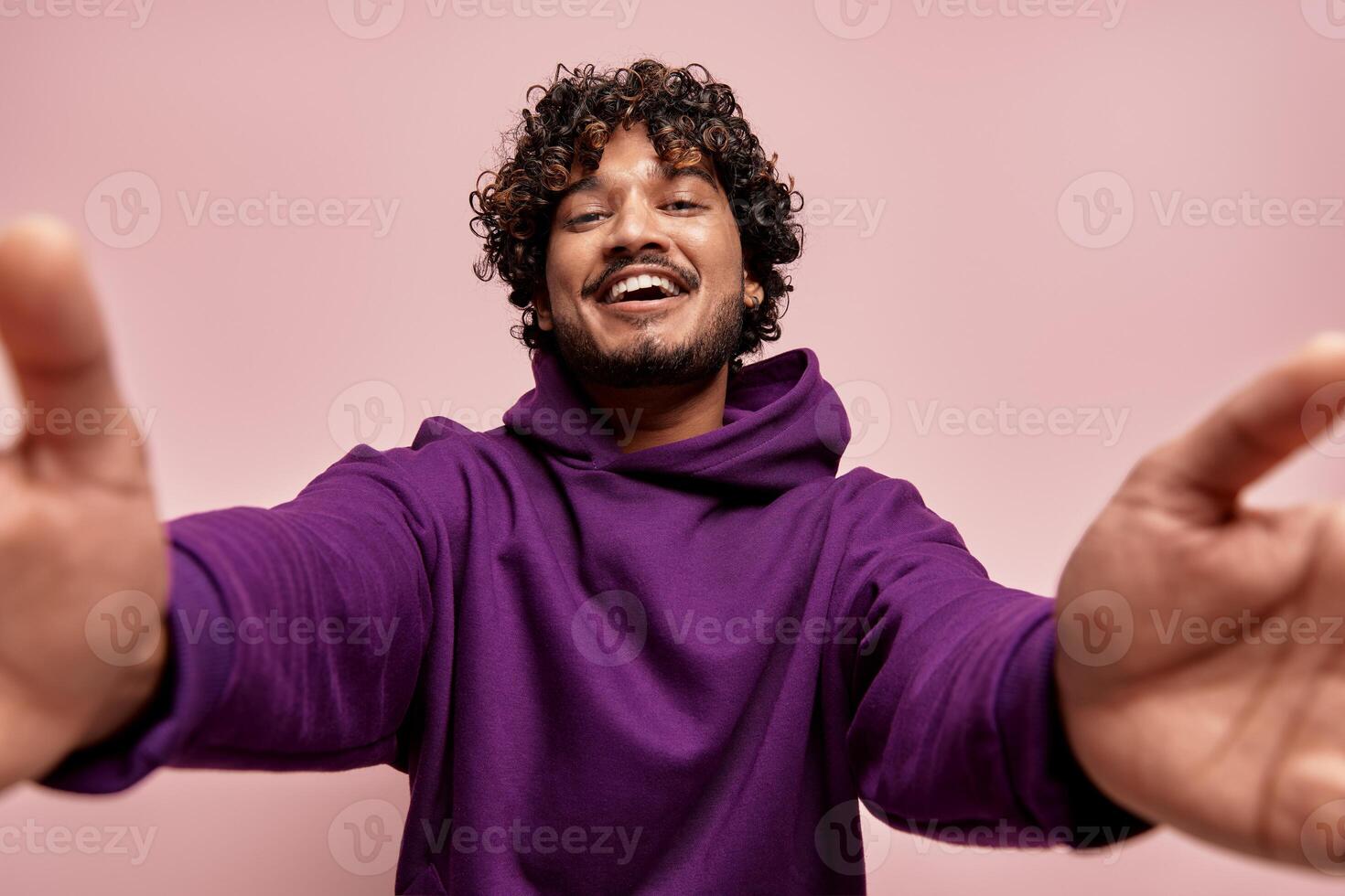 Low angle view of happy young Indian man stretching out hands against pink background photo