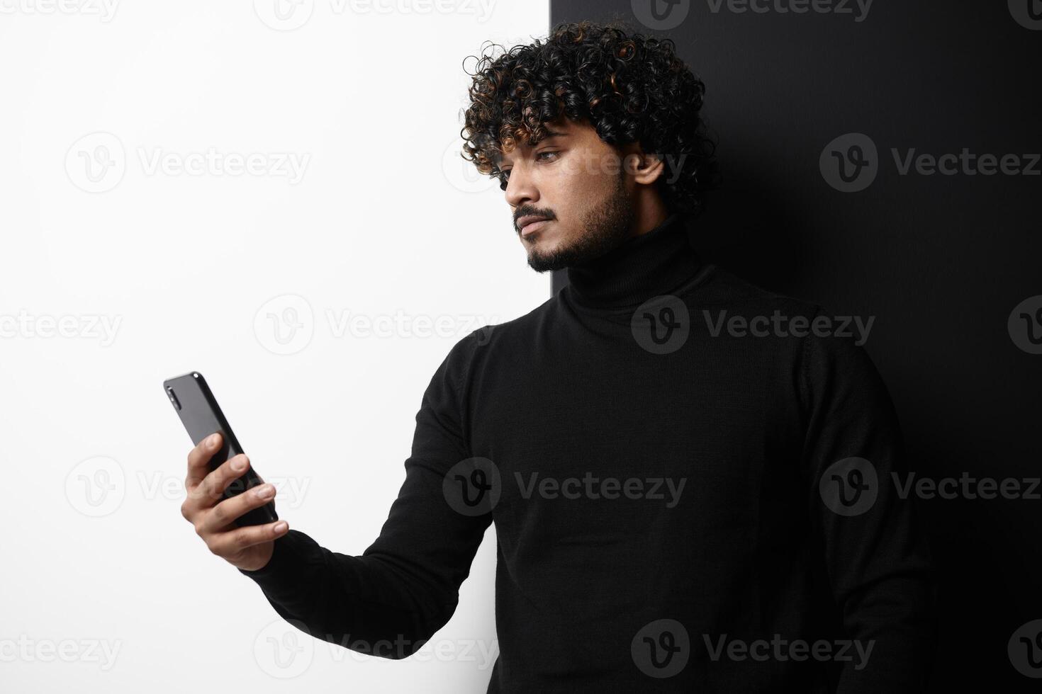 Handsome Indian man using smart phone while standing against black and white background photo