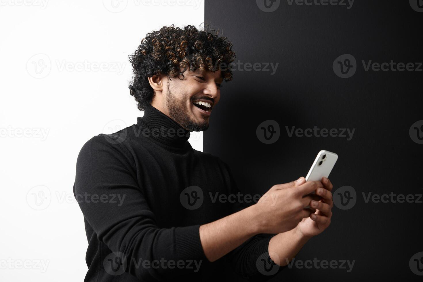 Happy Indian man using smart phone while standing against black and white background photo